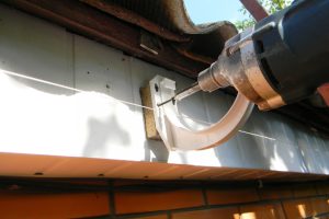 Contractor installing plastic roof gutter holder